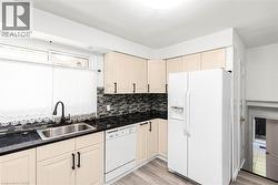 Kitchen featuring cream-colored cabinetry, dark countertops, a mosaic tile backsplash, and wood-finish flooring - 
