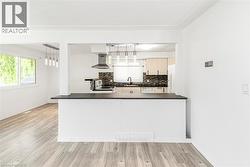 Open-concept kitchen featuring a breakfast bar with a dark countertop, white cabinetry, a stainless steel range hood, and a dark tile backsplash - 