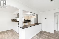 Open-concept kitchen and dining area featuring wood-finish flooring, a breakfast bar with a dark countertop, and a contemporary linear pendant light fixture - 
