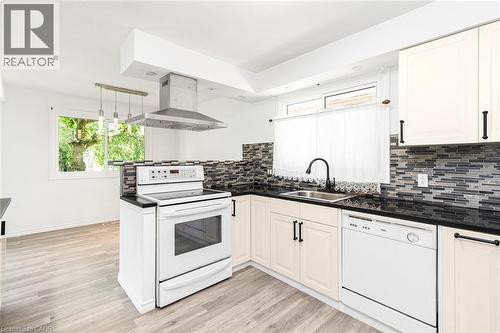 Kitchen featuring light-tone wood-finish flooring, white appliances, dark countertops, and a mosaic tile backsplash - 100 Mountain Avenue N, Hamilton, ON - Indoor Photo Showing Kitchen
