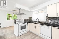 Kitchen featuring light-tone wood-finish flooring, white appliances, dark countertops, and a mosaic tile backsplash - 