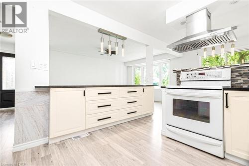 Kitchen featuring light wood-finish flooring, cream-colored cabinetry with dark hardware, a white range, a stainless steel range hood, and a dark countertop - 100 Mountain Avenue N, Hamilton, ON - Indoor Photo Showing Kitchen