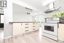 Kitchen featuring light wood-finish flooring, cream-colored cabinetry with dark hardware, a white range, a stainless steel range hood, and a dark countertop - 