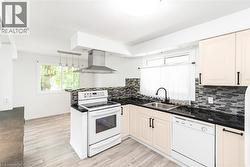 Kitchen featuring light wood-finish flooring, white cabinetry with black hardware, black countertops, and a mosaic tile backsplash - 