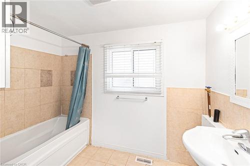 Bathroom featuring a built-in tub with tile surround, a single window with blinds, and a pedestal sink - 100 Mountain Avenue N, Hamilton, ON - Indoor Photo Showing Bathroom