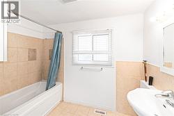 Bathroom featuring a built-in tub with tile surround, a single window with blinds, and a pedestal sink - 