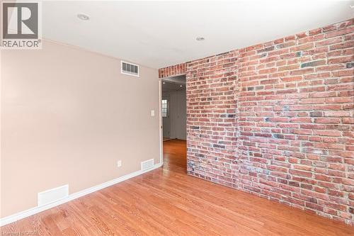 Exposed brick accent wall with recessed lighting, light-toned wall paint, wood-finish flooring, and white baseboards - 100 Mountain Avenue N, Hamilton, ON - Indoor Photo Showing Other Room