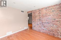 Exposed brick accent wall with recessed lighting, light-toned wall paint, wood-finish flooring, and white baseboards - 
