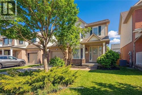 Light brick and neutral siding exterior with dark shutters, covered porch entry, mature front tree, and a manicured lawn - 5147 Ravine Crescent, Burlington, ON - Outdoor
