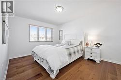 Bright bedroom featuring wood-finish flooring, a large window with blinds, and a built-in ceiling light fixture - 