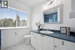 Bathroom featuring a broad window, white vanity with cabinet storage, integrated sink, and a blue countertop - 