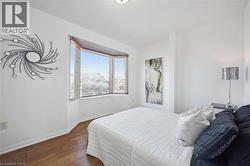 Room featuring a bay window with horizontal blinds, wood-finish flooring, and white baseboards - 