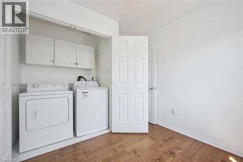 Dedicated laundry area featuring a built-in closet, white cabinetry, and wood-finish flooring - 5147 Ravine Crescent, Burlington, ON - Indoor Photo Showing Laundry Room