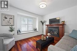 Living space featuring rich wood-finish flooring, a built-in window seat with plantation shutters, a fireplace with a wood mantel, and a flush mount ceiling light fixture - 