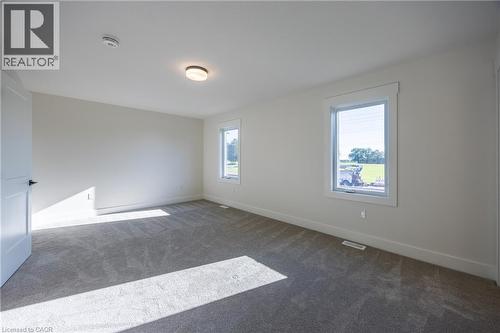 Carpeted room featuring two windows with white trim, a flush-mount ceiling light fixture, and a solid interior door with black hardware - 111 Amber Street, Waterford, ON - Indoor Photo Showing Other Room