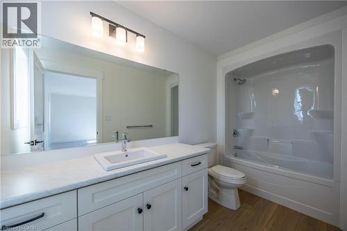 Bathroom featuring a white vanity with an undermount sink, a large frameless mirror, a three-light vanity fixture, a white toilet, and a white tub/shower combination - 111 Amber Street, Waterford, ON - Indoor Photo Showing Bathroom