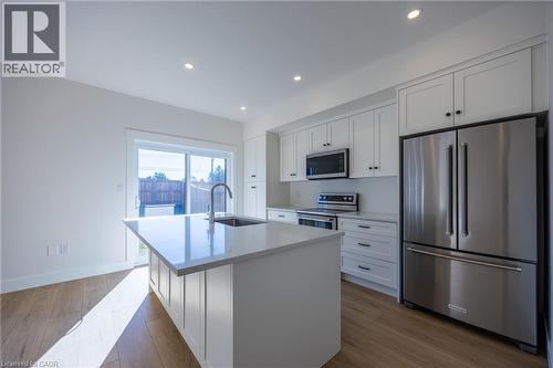 Modern kitchen featuring a central island with an undermount sink, stainless steel appliances, white cabinetry, recessed lighting, and wood-finish flooring - 115 Amber Street, Waterford, ON - Indoor Photo Showing Kitchen