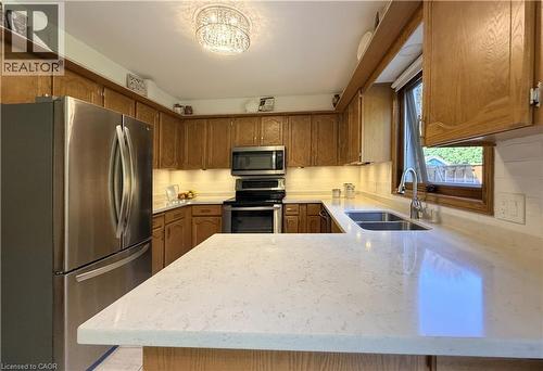 U-shaped kitchen featuring wood cabinetry, quartz countertops, and a white subway tile backsplash. - 7 Mann Avenue, Simcoe, ON - Indoor Photo Showing Kitchen With Stainless Steel Kitchen With Double Sink