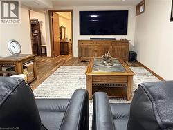 Spacious living area featuring wood-finish flooring, a large area rug, and a wood media console - 