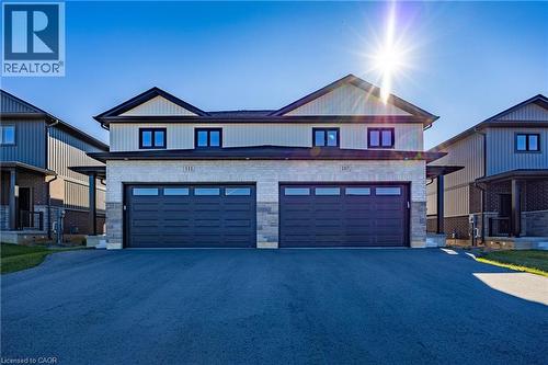 Contemporary duplex featuring light-colored siding, stone accents, black-framed windows, and two large garage doors with horizontal glass panels - 107 Amber Street, Waterford, ON - Outdoor With Facade