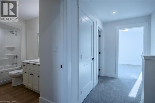 Bathroom featuring a white vanity with a rectangular undermount sink, a white countertop, wood-finish flooring, a white toilet, and a white tub with shower - 107 Amber Street, Waterford, ON - Indoor Photo Showing Bathroom