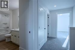 Bathroom featuring a white vanity with a rectangular undermount sink, a white countertop, wood-finish flooring, a white toilet, and a white tub with shower - 