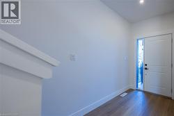 Entryway featuring wood-finish flooring, white baseboards, a white paneled door with a black handle, and an adjacent full-length vertical window - 
