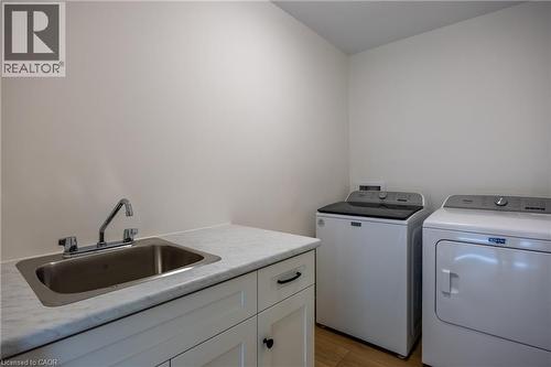 Laundry area featuring a utility sink with chrome faucet, light-toned countertop, white cabinetry with dark hardware, and wood-finish flooring - 107 Amber Street, Waterford, ON - Indoor Photo Showing Laundry Room