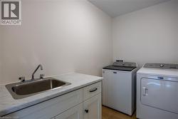 Laundry area featuring a utility sink with chrome faucet, light-toned countertop, white cabinetry with dark hardware, and wood-finish flooring - 