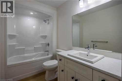 Bathroom featuring a white integrated tub and shower unit, a rectangular drop-in sink, a light-colored countertop, and a vanity with white cabinetry and dark hardware - 107 Amber Street, Waterford, ON - Indoor Photo Showing Bathroom