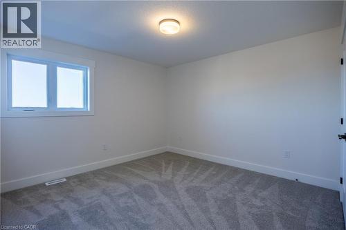 Neutral tone carpeted room featuring white trim, a single window with white framing, a flush mount ceiling light fixture, and a white interior door with matte black hardware - 107 Amber Street, Waterford, ON - Indoor Photo Showing Other Room