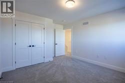 Spacious room featuring neutral carpeting, white trim, and a contemporary ceiling light fixture - 