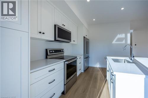 Modern kitchen featuring white shaker cabinetry, stainless steel appliances, light wood-finish flooring, recessed lighting, and an island with an undermount sink - 107 Amber Street, Waterford, ON - Indoor Photo Showing Kitchen With Upgraded Kitchen