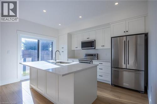 Modern kitchen featuring white shaker cabinetry, stainless steel appliances, a center island with an undermount sink, recessed lighting, and wood-finish flooring - 107 Amber Street, Waterford, ON - Indoor Photo Showing Kitchen