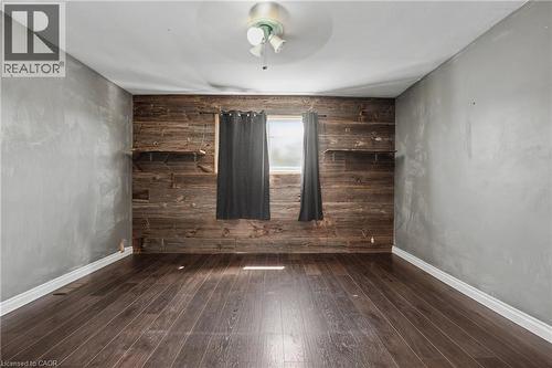 Room featuring wood-finish flooring, a rustic wood accent wall with integrated shelving, and light gray painted walls - 485 Cochrane Road, Hamilton, ON - Indoor Photo Showing Other Room