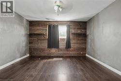 Room featuring wood-finish flooring, a rustic wood accent wall with integrated shelving, and light gray painted walls - 