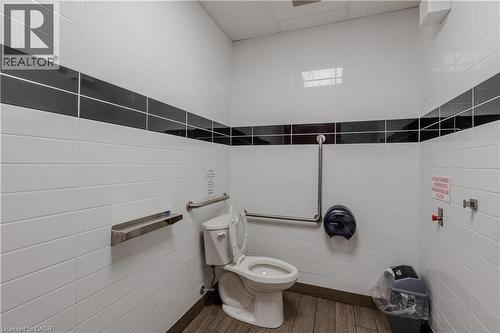 Restroom featuring white rectangular wall tiles with a black accent band, wood-finish flooring, and stainless steel grab bars - 96 Gerrard St E, Toronto, ON 