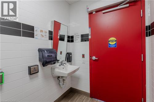 Restroom featuring white subway tile with black accent bands, a red door with an automatic opener, and a wall-mounted sink with chrome fixtures - 96 Gerrard St E, Toronto, ON 