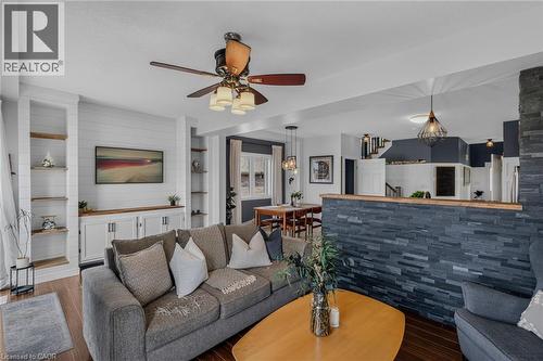 Living area featuring dark wood-finish flooring, a built-in entertainment center with shiplap backing, integrated shelving, and a ceiling fan - 174 Woodway Trail, Simcoe, ON - Indoor Photo Showing Living Room