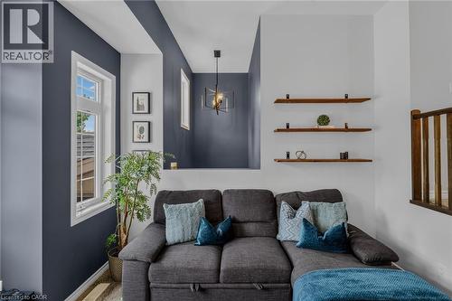 Living area featuring a distinct accent wall, multiple windows with white trim, a decorative pendant light fixture, and three wall-mounted wood-finish shelves - 174 Woodway Trail, Simcoe, ON -  Photo Showing Living Room