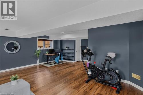 Spacious lower-level room featuring wood-finish flooring, recessed lighting, a window with horizontal blinds, and built-in shelving - 174 Woodway Trail, Simcoe, ON - Indoor Photo Showing Other Room