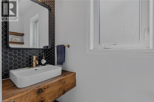 Floating wood-finish vanity with a rectangular basin sink and wall-mounted brass faucet - 174 Woodway Trail, Simcoe, ON - Indoor Photo Showing Bathroom