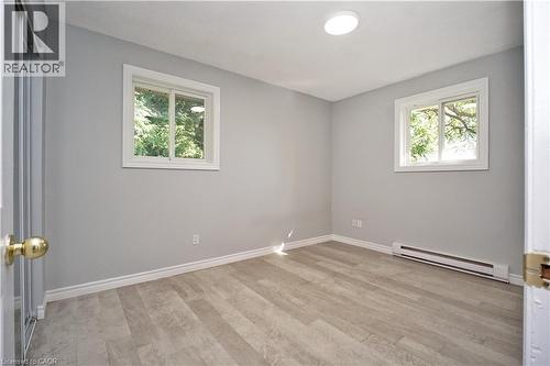 Room featuring neutral gray walls, wood-finish flooring, two windows with white trim, and a ceiling-mounted light fixture - 119 Cedar Street S Unit# 14, Kitchener, ON - Indoor Photo Showing Other Room