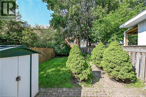 Landscaped backyard featuring a paver stone pathway, mature manicured evergreens, a wooden privacy fence, a storage shed, and a lush green lawn - 155 Newlands Avenue, Hamilton, ON - Outdoor