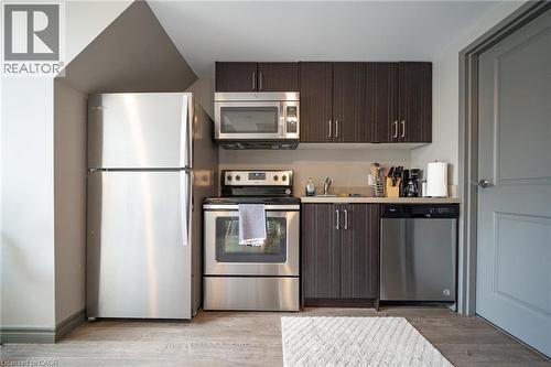 Compact kitchen featuring a full suite of stainless steel appliances, wood-finish flooring, dark wood cabinetry, and light-toned countertops - 321 Spruce Street Unit# 710, Waterloo, ON - Indoor Photo Showing Kitchen With Stainless Steel Kitchen
