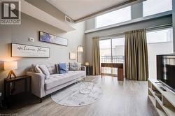 Living space featuring high ceilings, wood-finish flooring, a full wall of windows, and a glass sliding door opening to a balcony - 