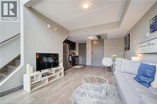 Open-concept living area featuring wood-finish flooring, a contemporary staircase with metal railing, and a kitchen area with stainless steel appliances - 321 Spruce Street Unit# 710, Waterloo, ON - Indoor Photo Showing Living Room