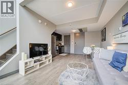 Open-concept living area featuring wood-finish flooring, a contemporary staircase with metal railing, and a kitchen area with stainless steel appliances - 