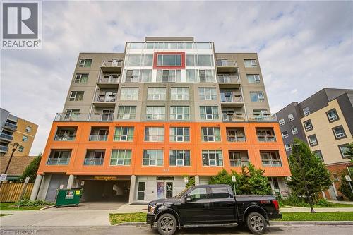 Modern multi-story building featuring a facade with orange and gray panels, multiple balconies, and an integrated ground-level parking garage - 321 Spruce Street Unit# 710, Waterloo, ON - Outdoor With Facade