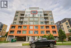 Modern multi-story building featuring a facade with orange and gray panels, multiple balconies, and an integrated ground-level parking garage - 